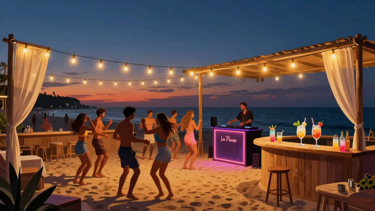 People dancing barefoot on a beach at La Plage under string lights, with cocktails and the sea in the background.